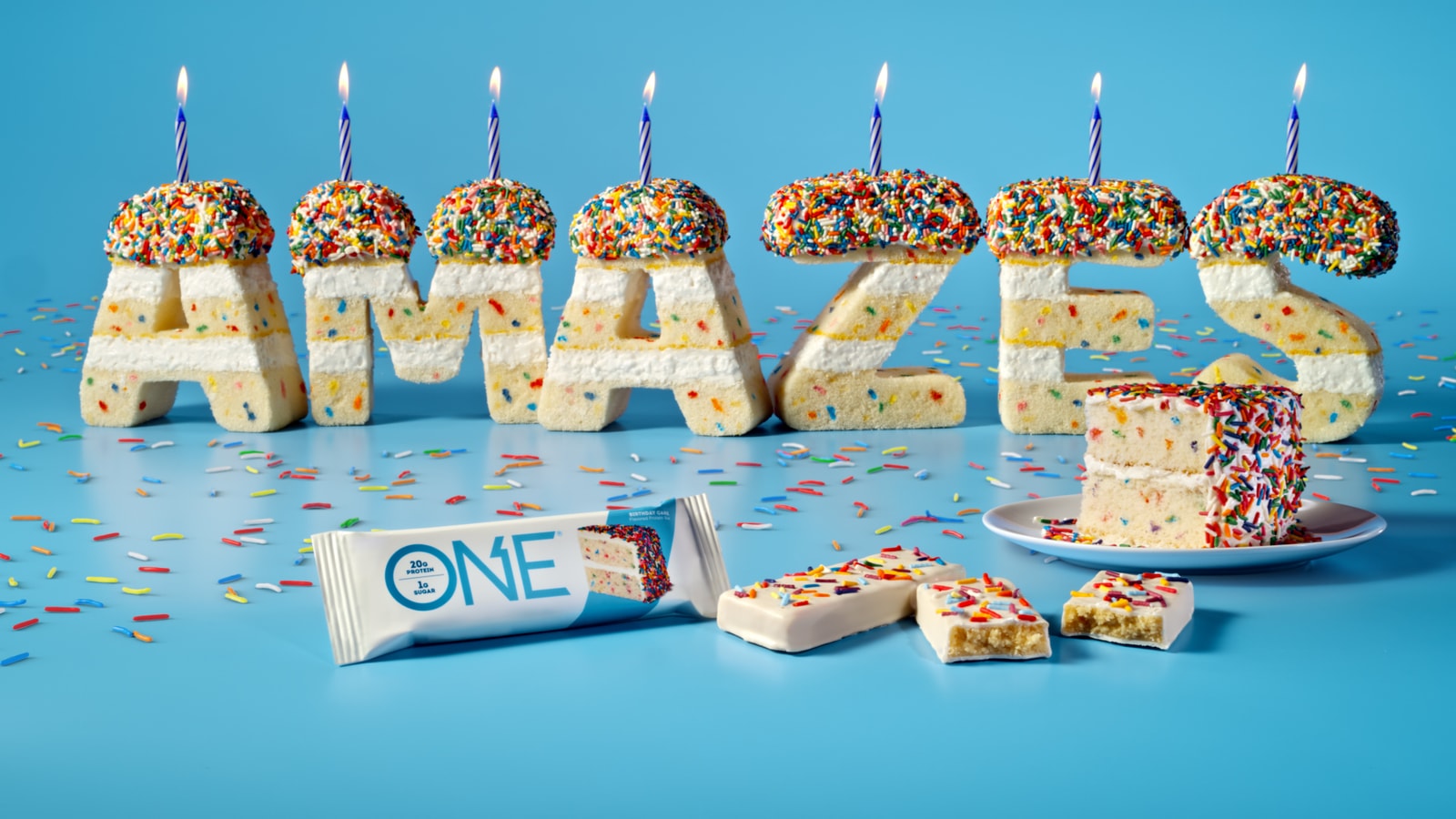 Birthday cake letters spell “AMAZES” above ONE protein bars.