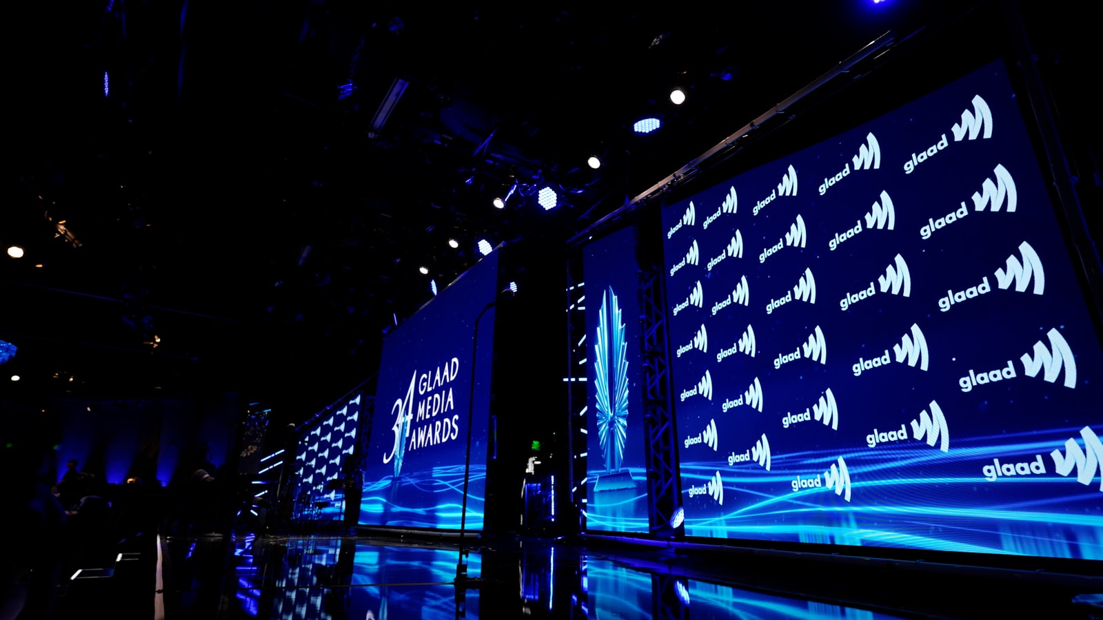 Blue stage screens display repeated GLAAD logos and the awards identity.