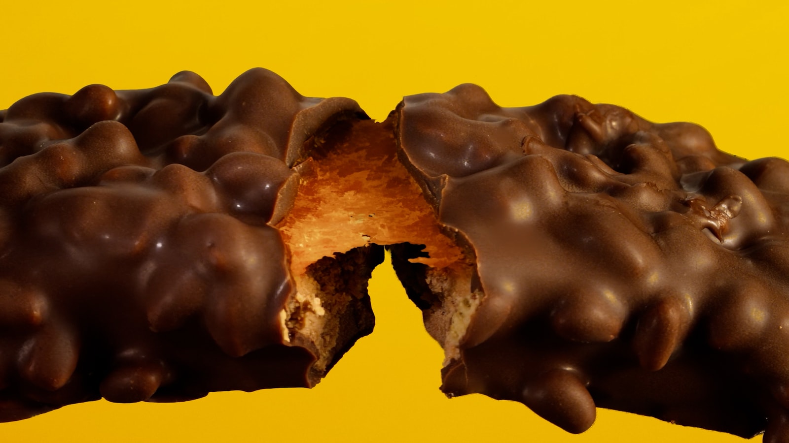A chocolate-coated Fulfil bar breaks open against a yellow background.