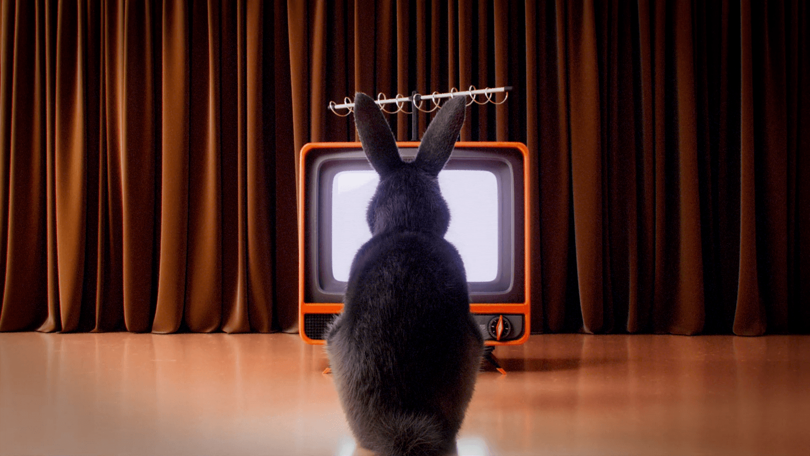 A rabbit faces an orange television on a theater stage.
