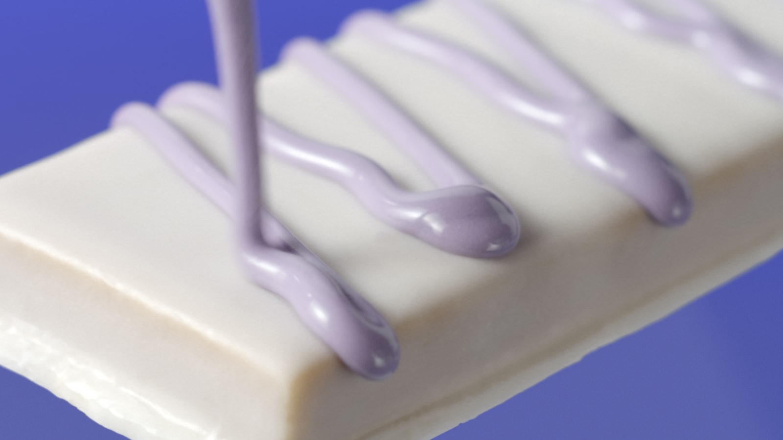Purple icing drizzles over a white chocolate-coated ONE bar.