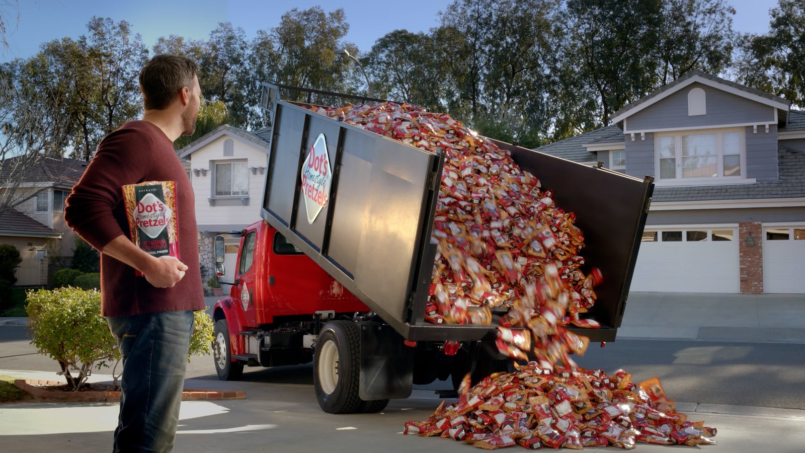 A dump truck unloads Dot’s pretzel bags beside a man in a driveway.