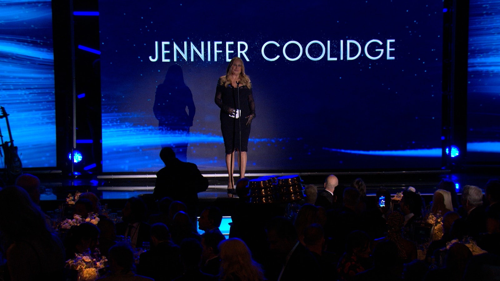 A presenter stands beneath the name Jennifer Coolidge on the 2023 GLAAD stage.