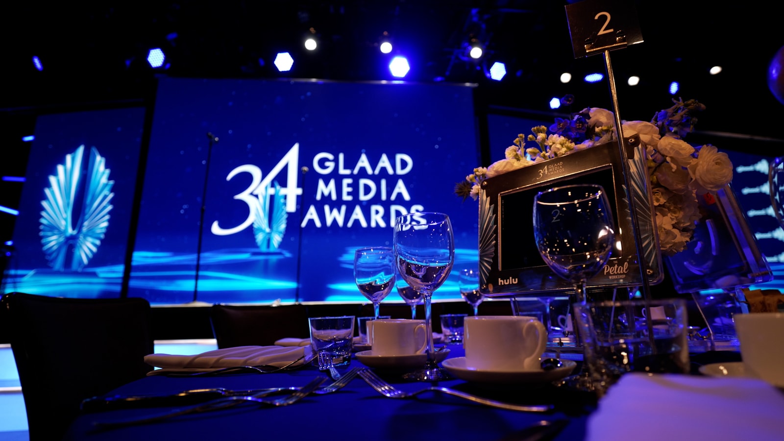 A banquet table faces the blue 34th GLAAD Media Awards stage.
