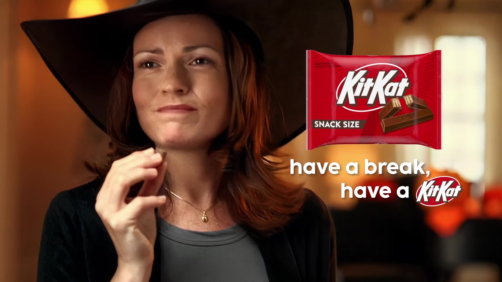 A woman in a witch costume enjoys a KitKat beside the updated snack-size packaging.