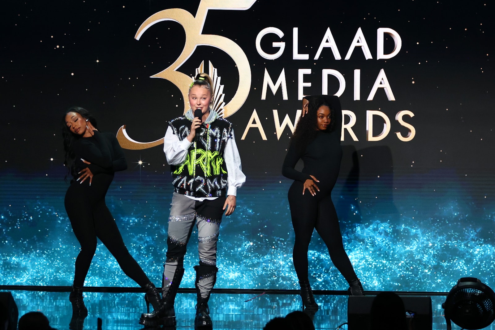 A singer and dancers perform before the 35th GLAAD Media Awards logo.