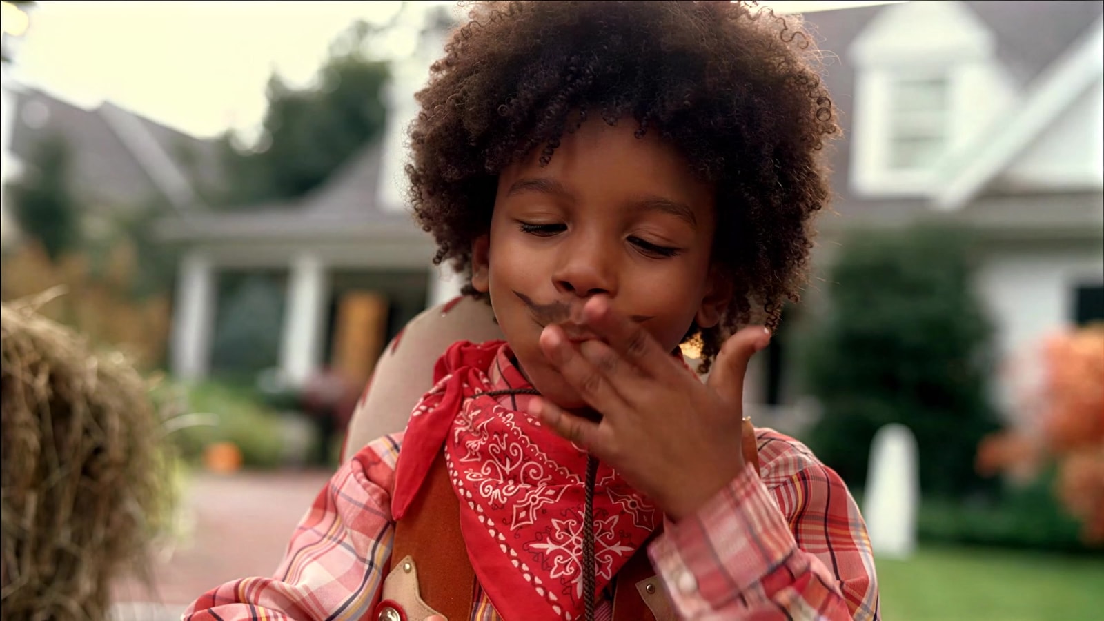 A child in a cowboy costume enjoys a KitKat outside a house.