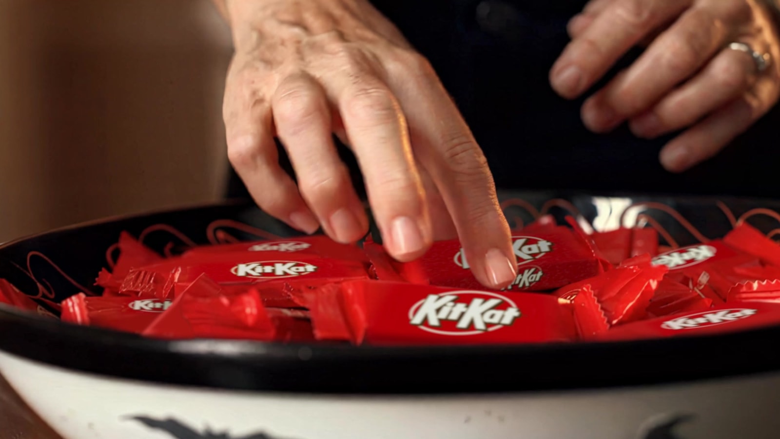 A hand reaches into a bowl filled with red-wrapped KitKat bars.