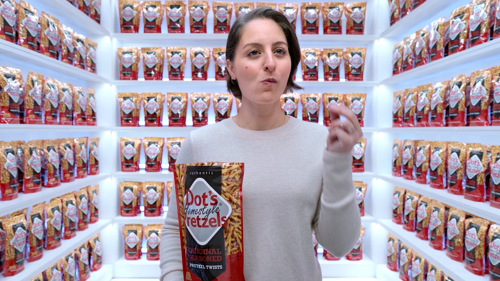 A woman holds Dot’s pretzels inside a pantry lined with pretzel bags.