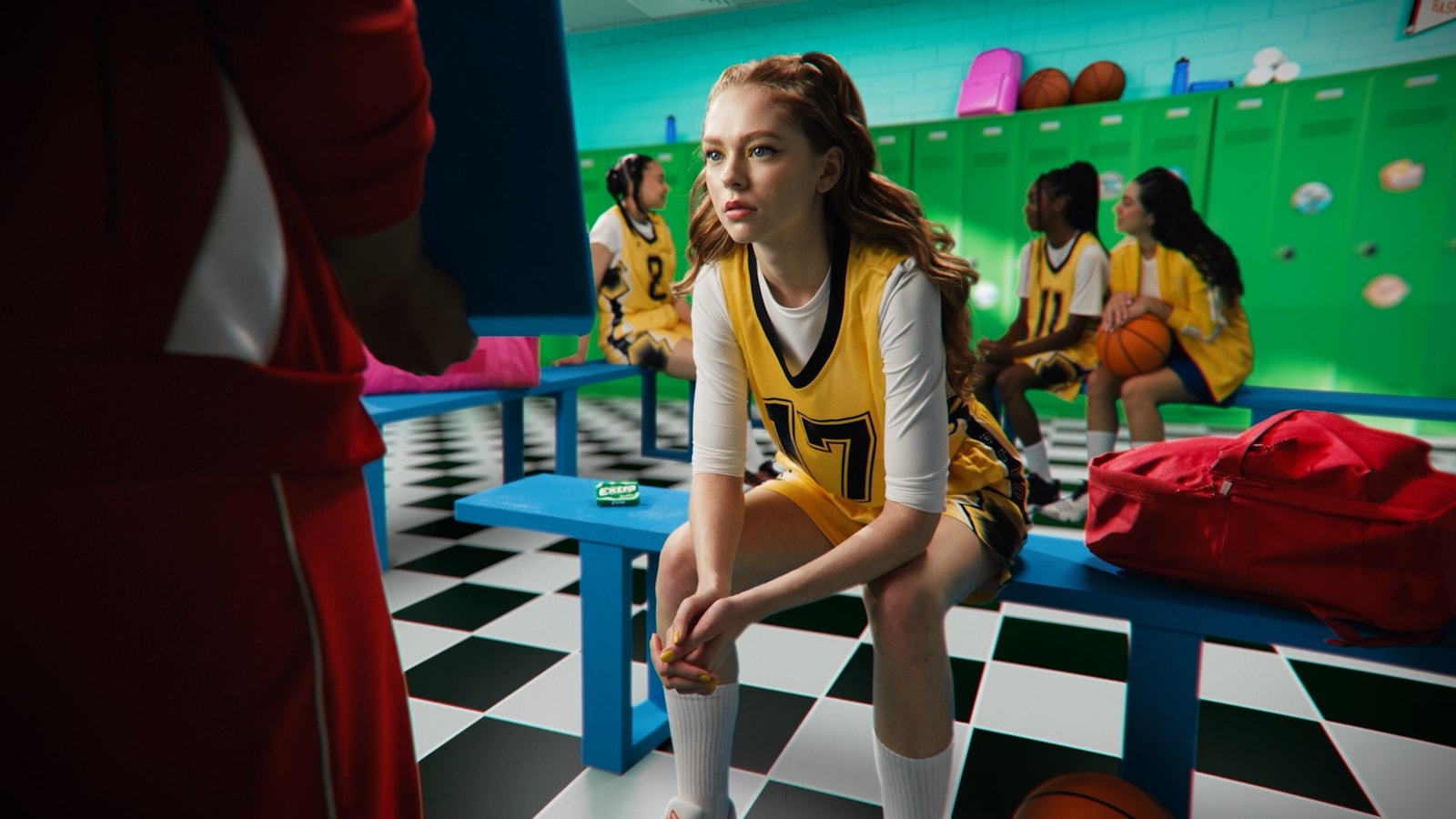 A basketball player sits in a green locker room.