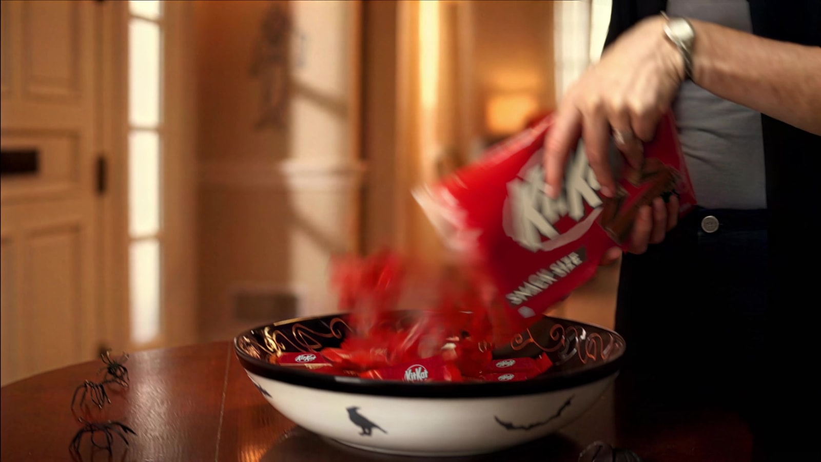 KitKat candies pour from a red bag into a Halloween candy bowl.